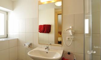A modern bathroom with a sink, a shower, and a toilet. The walls are brightly tiled, and a mirror reflects the light.