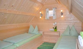 A cozy room with wooden paneling and two single beds. The colors are bright and friendly, with a small plant on the table.