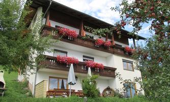 A charming house with balconies adorned with colorful flowers. Surrounded by green meadows and apple trees, it exudes a cozy atmosphere.