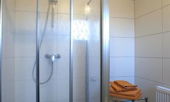 A modern shower with a glass partition and a stack of towels on a small table. Neat, bright tiles adorn the walls.