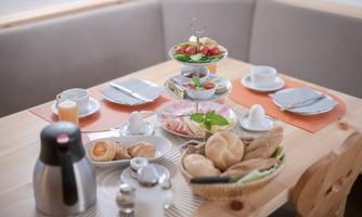 A beautifully set table with a selection of food and drinks.  
There is fresh bread, fruit, and a pot of coffee.