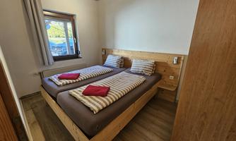 A simple room with two single beds and wood paneling. There are bright curtains and a window that lets in natural light.