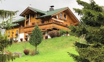 A beautiful wooden house on a hill, surrounded by green trees. The sky is cloudy, giving the scene a calm atmosphere.