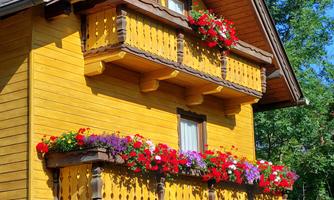 A beautiful yellow wooden house with two balconies. Colorful flowers are blooming on the balconies.