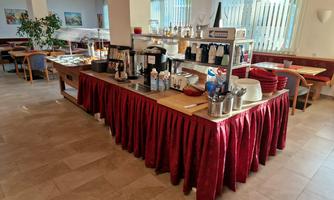 A buffet in a restaurant with several hot beverages and plates. The table is covered with a red cloth and the surroundings are bright and inviting.