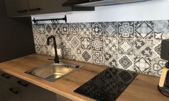 A modern kitchen with a wooden worktop and an elegant tiled backsplash. The sink and an electric cooktop are visible.