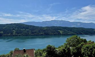 A tranquil lake surrounded by green mountains and a radiant sky. The landscape appears peaceful and inviting.