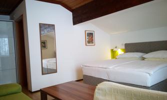 A cozy bedroom with a double bed and wooden beam ceiling. There is a small table and a seating area with a green sofa.