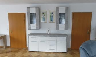 A modernly furnished room with a white sideboard and two doors. Two pictures are hanging on the wall, and the floor is made of wood.