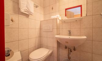 A small bathroom with white tiles. There is a sink, a toilet, and a mirror above the sink.