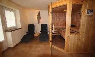 A cozy wellness area with a wooden sauna and two loungers. The room has large windows and a warm, inviting atmosphere.