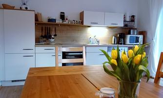 A modern kitchen with white cabinets and wooden shelves. On the table, there is a vase with yellow tulips.