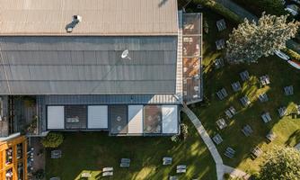 A view from above of a modern building with a green outdoor area. The garden features several loungers and pathways.