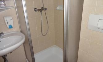 A modern bathroom with a shower cabin and a sink. The walls are tiled in a light shade.