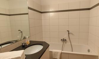 A modern bathroom with a bathtub and a large mirror. The walls are covered with white tiles, and there are fresh towels on the black shelf.