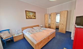 A cozy bedroom with a double bed and wooden wardrobes. The room is bright and friendly designed, with a blue floor and decorative elements.