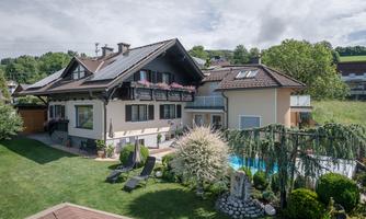 A beautiful house with a well-kept garden and a pool. In the foreground, there are loungers for relaxation.