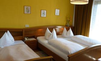 A bright room with yellow walls and wooden furniture. There are two beds with white pillows and fresh flowers on the nightstand.