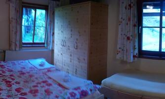 A cozy bedroom with a double bed and floral bedding. Large windows let in plenty of daylight and offer a view of the outdoors.