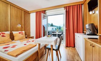 A cozy room with wood paneling and two beds. Large windows offer a view of the balcony and the surroundings.