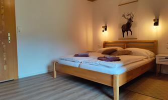 A cozy bedroom with a double bed and wooden details. A deer motif hangs on the wall, and there is soft lighting.