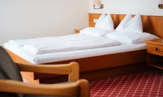 A cozy bedroom with a double bed and white bedding. Pictures of flowers are hanging on the wall.