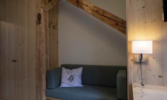 A cozy living area with a green sofa and a cushion. The walls are made of light wood and there is a lamp next to the sofa.