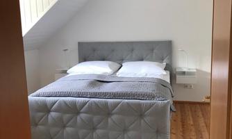 A modern bedroom with a gray bed and white bedding. The wooden floor and the carpet create a cozy atmosphere.