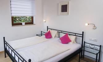 A cozy bedroom with a black metal bed and two white beds. There are pink pillows and a modern nightstand.