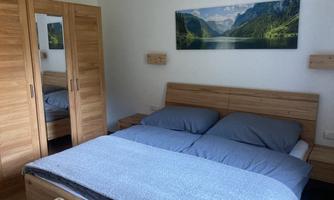 A modern bedroom with a large double bed and wooden furniture. On the wall hangs a landscape painting of mountains and a lake.