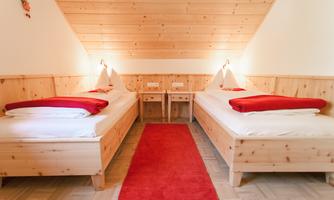 A cozy bedroom with two beds and red bedding. The room is decorated with wooden paneling and a red carpet.