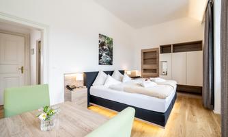 A cozy bedroom with a large bed and modern furniture. The room has a bright, inviting atmosphere and a small dining area.