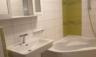A modern bathroom with a shower, a bathtub, and a sink. The walls are decorated with white tiles and green accents.