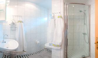 A modern bathroom with white tiles and an elegant shower. Two comfortable bathrobes are hanging ready.