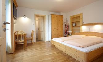 A cozy room with a double bed and wooden floor. There is a small table and chairs as well as a wardrobe.