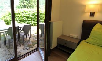 A cozy bedroom with a green bed and access to a terrace. Outside are chairs and a beautiful view of nature.