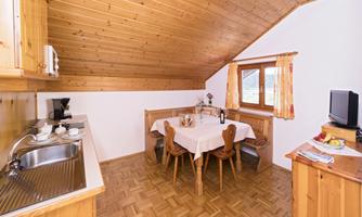 A cozy kitchen corner with wooden furniture and a round table. Daylight pours in through the window, creating an inviting atmosphere.