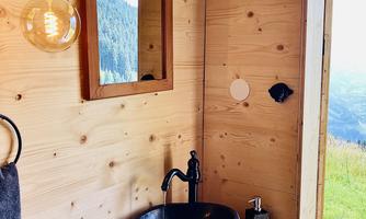 A modern bathroom with wood paneling and a stone sink. It includes a large mirror, towels, and a beautiful view of nature.