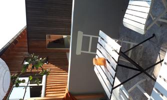 A cozy outdoor area with a small table and white chairs. In the background, a wooden facade and a window can be seen.