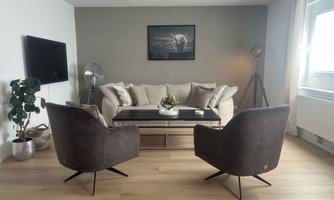 A modern living room with a comfortable sofa and two elegant armchairs. A coffee table in the middle and a plant complement the cozy atmosphere.