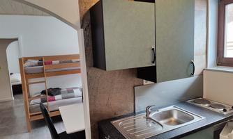 A modern kitchen unit with a sink and black furniture. In the background, two bunk beds are visible in a bright room.