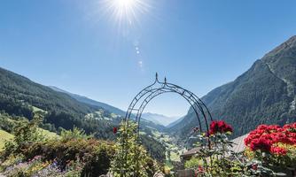 A beautiful mountain landscape with a garden arch and blooming flowers. The sun shines brightly over the green valley.