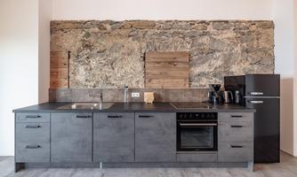 A modern kitchen with dark furniture and a natural stone wall. The equipment includes a stove, refrigerator, and various kitchen appliances.