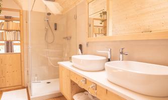 A bright and modern bathroom with wooden details. It features a glass shower and two sinks on a stylish vanity.