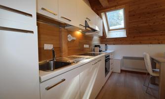 A modern kitchen with white cabinets and wood paneling. It features a sink, stove, and windows that provide plenty of natural light.