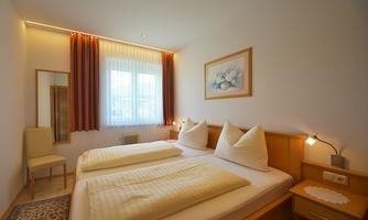 A cozy bedroom with two beds and bright curtains. The room is simply furnished and has a window with plenty of daylight.