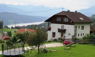 A picturesque house in the greenery with a view of a lake and mountains in the background. The garden has a trampoline and a calm, rural atmosphere.
