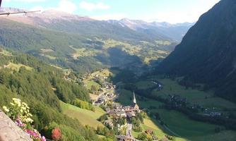 A picturesque valley with gentle hills and a small village.  
Surrounded by high mountains and blue sky.