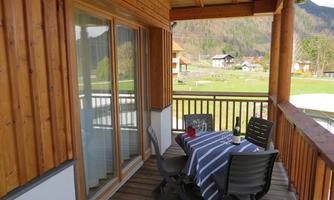 A cozy balcony with a table and chairs. In the background, a green landscape is visible.