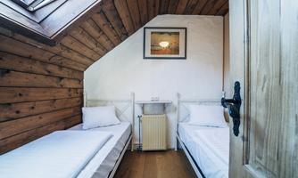 A cozy room with two single beds and wooden paneling. A window shaft lets in daylight and creates an inviting atmosphere.